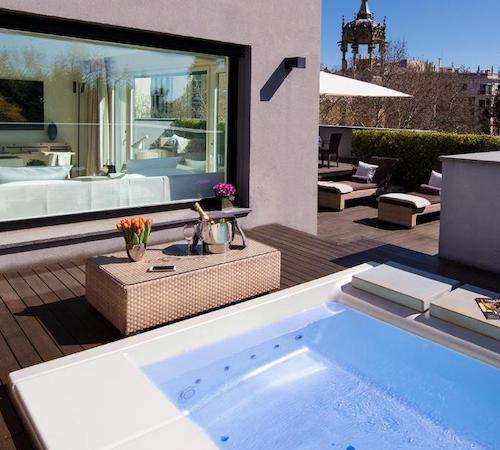 Jacuzzi exterior en la terraza con mobiliario y frente a una cristalera donde se puede ver la suite con la cama en el hotel ABaC Restaurant Hotel Barcelona GL Monumento