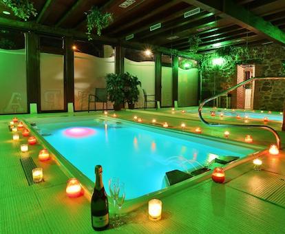 Foto de la piscina climatizada iluminada en el spa del Hotel Spa Casona La Hondonada con varias velas encendidas en el borde y una botella de cava cerca.