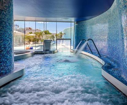 Piscina climatizada con chorros de agua para masajear y distintas zonas con agua con burbujas para relajarse en el interior.