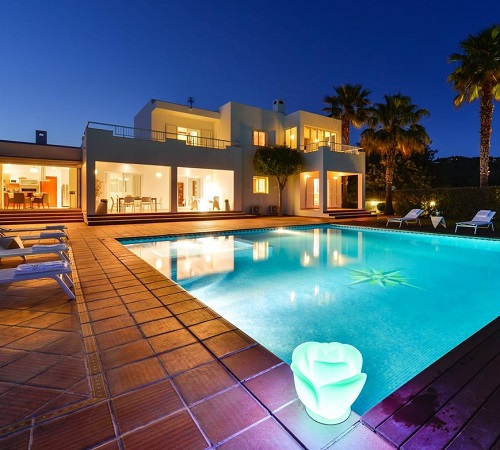 Foto de la piscina de noche donde se ve la Villa Can Fluxa con las luces encendidas y lineas rectas de la arquitectura